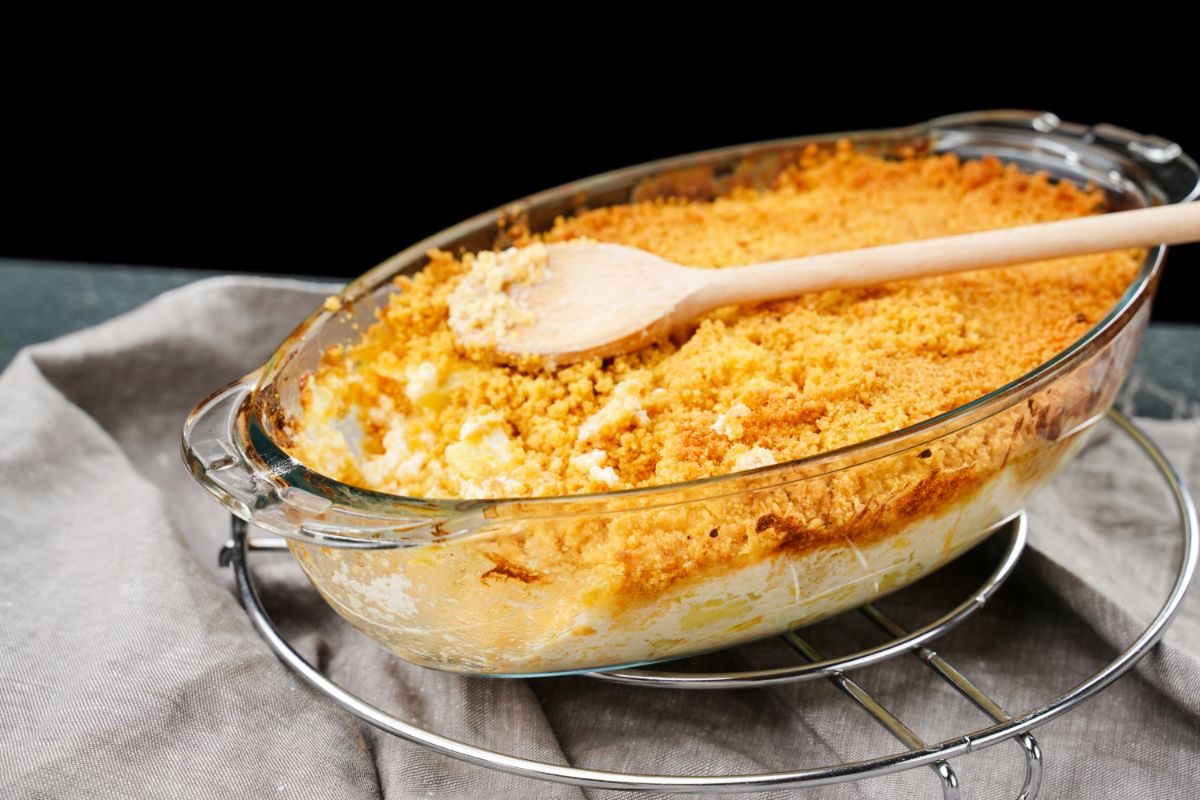 glass oval baking dish filled with funeral potatoes on table with gray napkin with wooden spoon on top