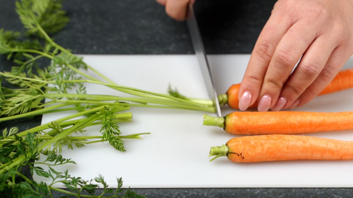 carrots on white cutting board having greens trimmed with knife