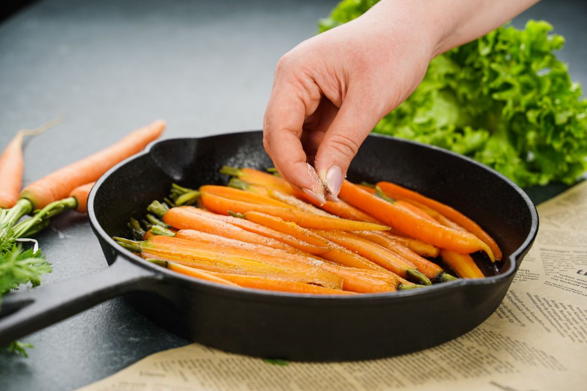 hand sprinkling herbs on top of carrots in skillet