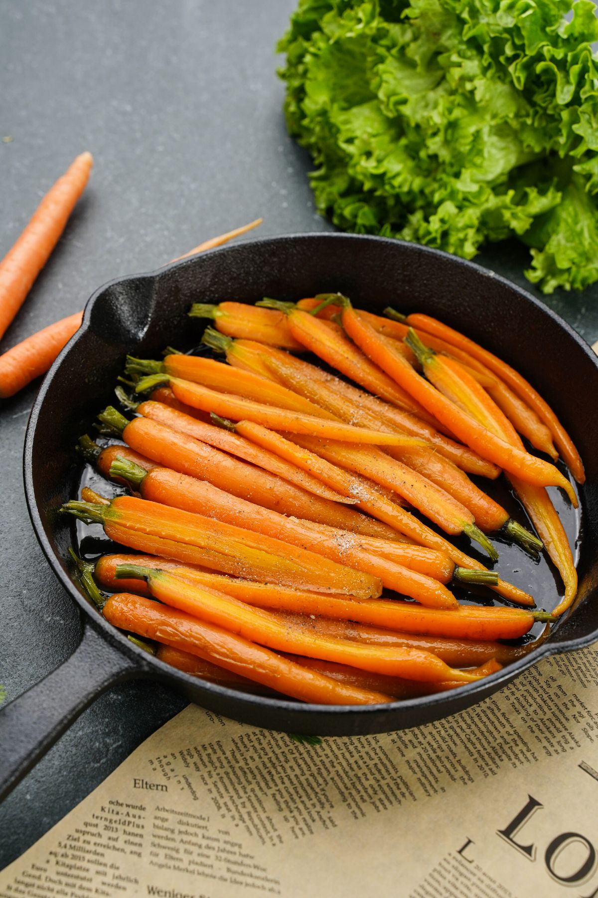 black cast iron skillet of carrots on gray table and newsprint
