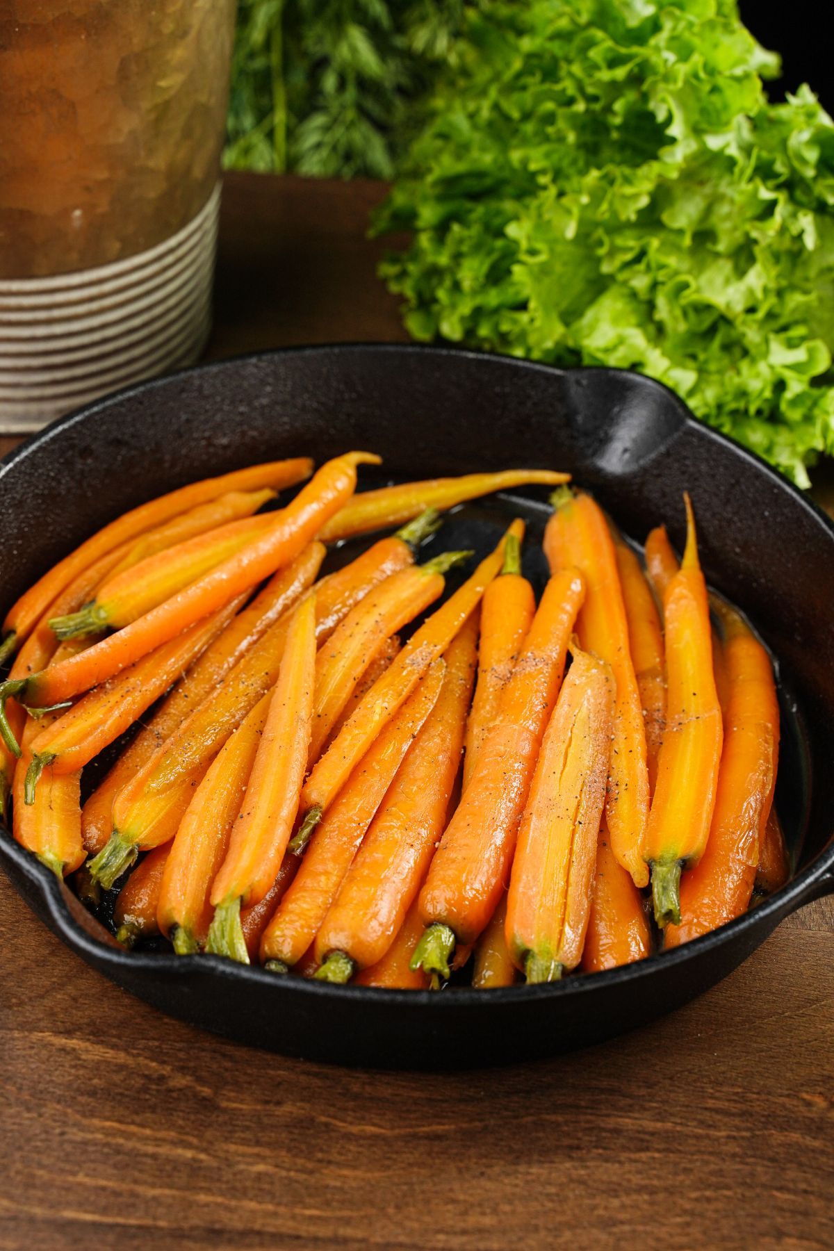 brown sugar glazed carrots in black skillet next to fresh herbs