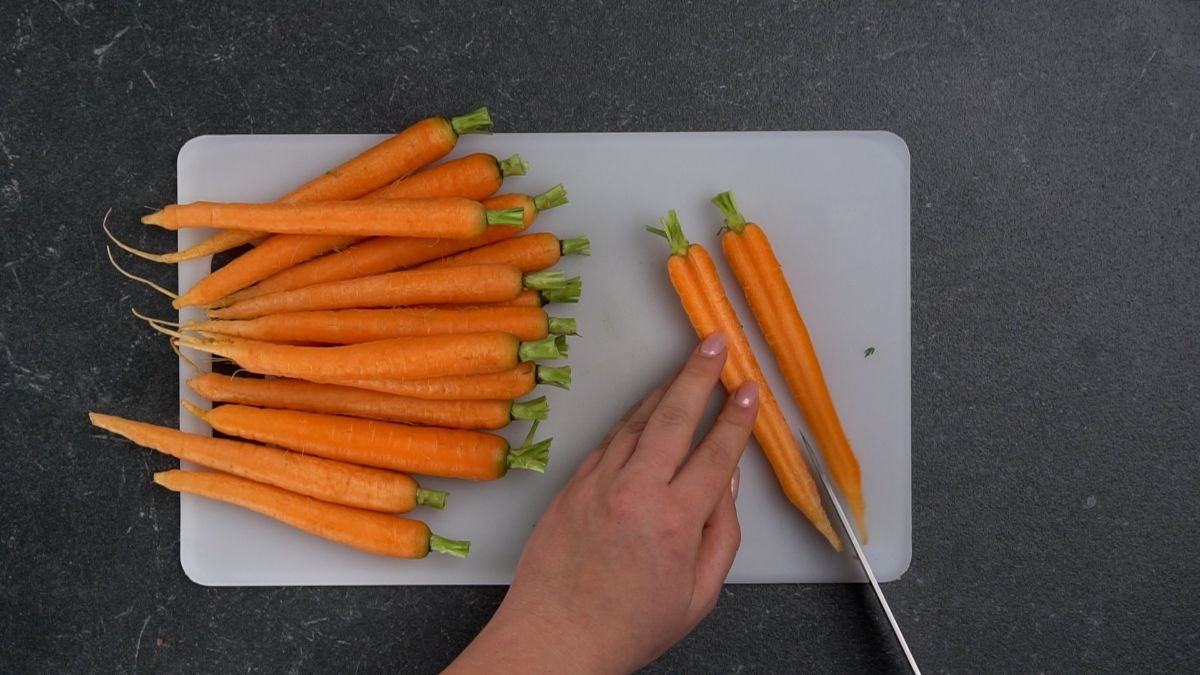 carrots on white cutting board being sliced in half