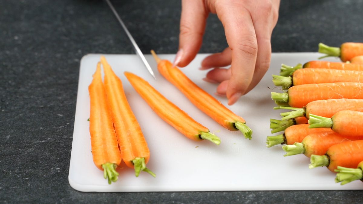 hands holding knife cutting young carrots in half lengthwise