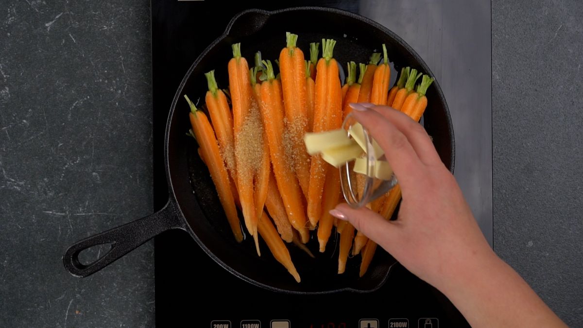 hand adding butter to skillet of carrots