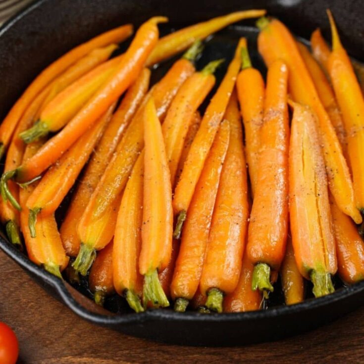 cooked young carrots in black cast iron skillet on wood table