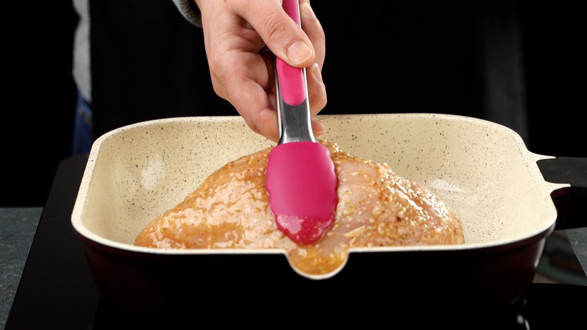 pink tongs placing chicken into grill pan
