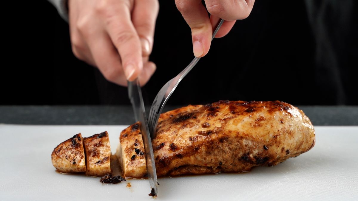 hand slicing chicken on white cutting board