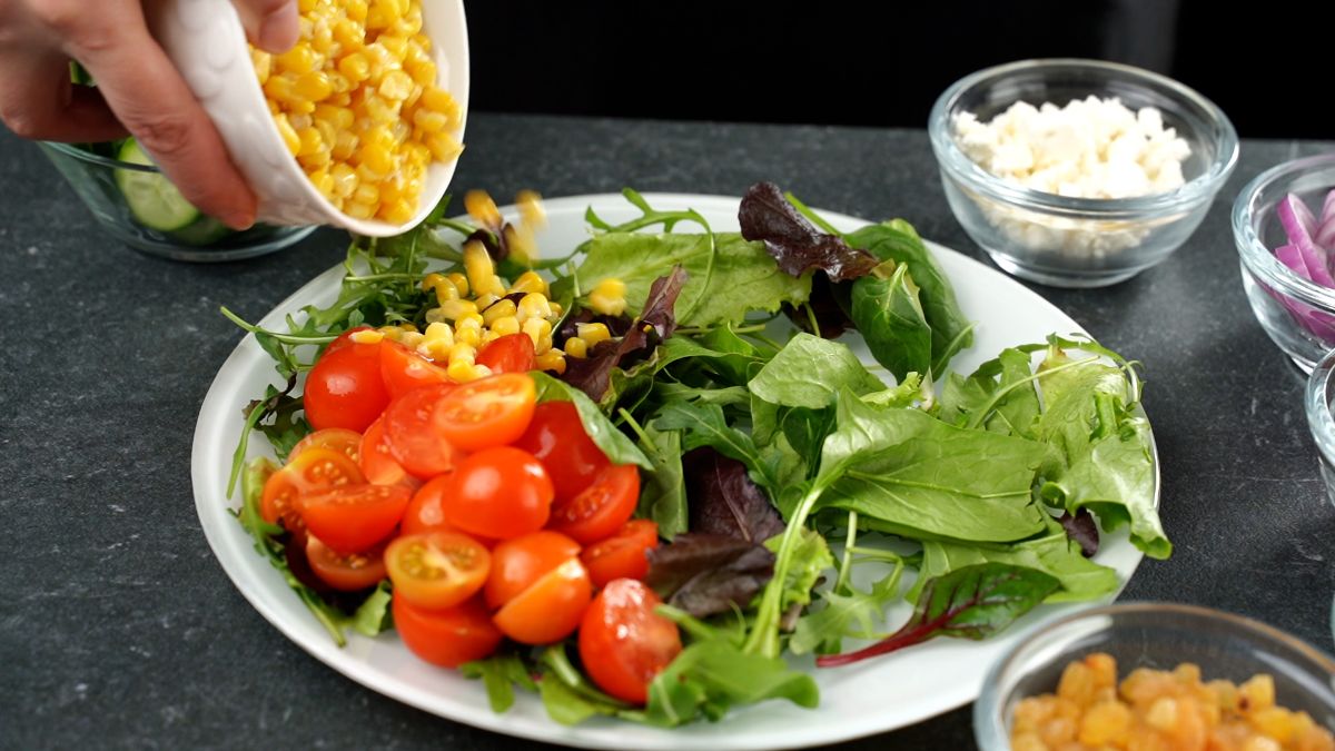 hand adding corn to plate of greens and tomatoes