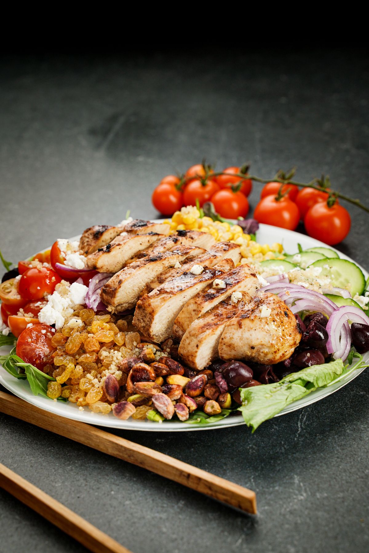 salad on white plate topped with chicken with tomatoes in background on gray table