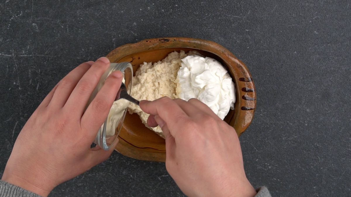 hand spooning horseradish out of clear bowl into wooden bowl