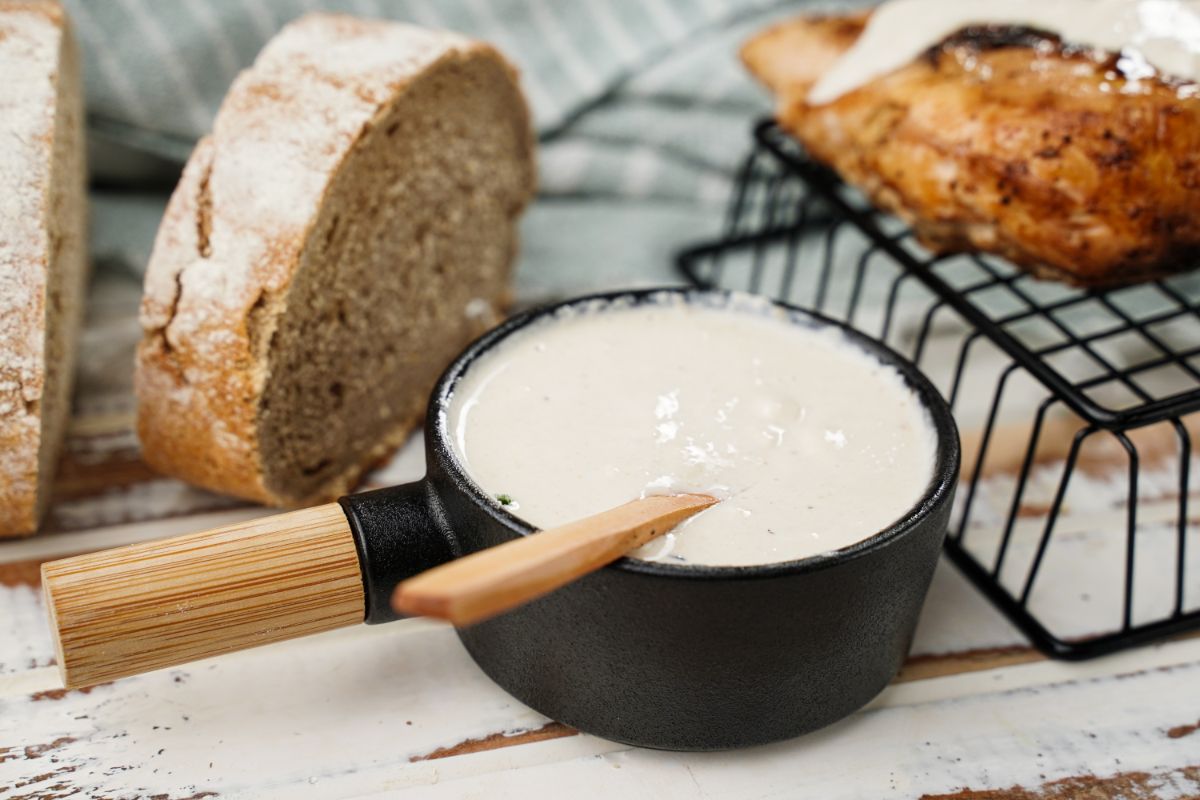 black soup bowl of white sauce with wooden spoon by sliced bread