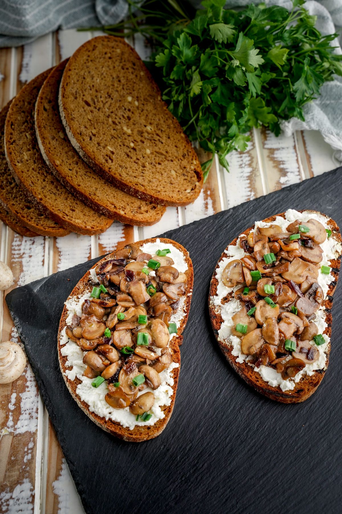 image looking down on black plate with two slices of mushroom ricotta toast on light wood