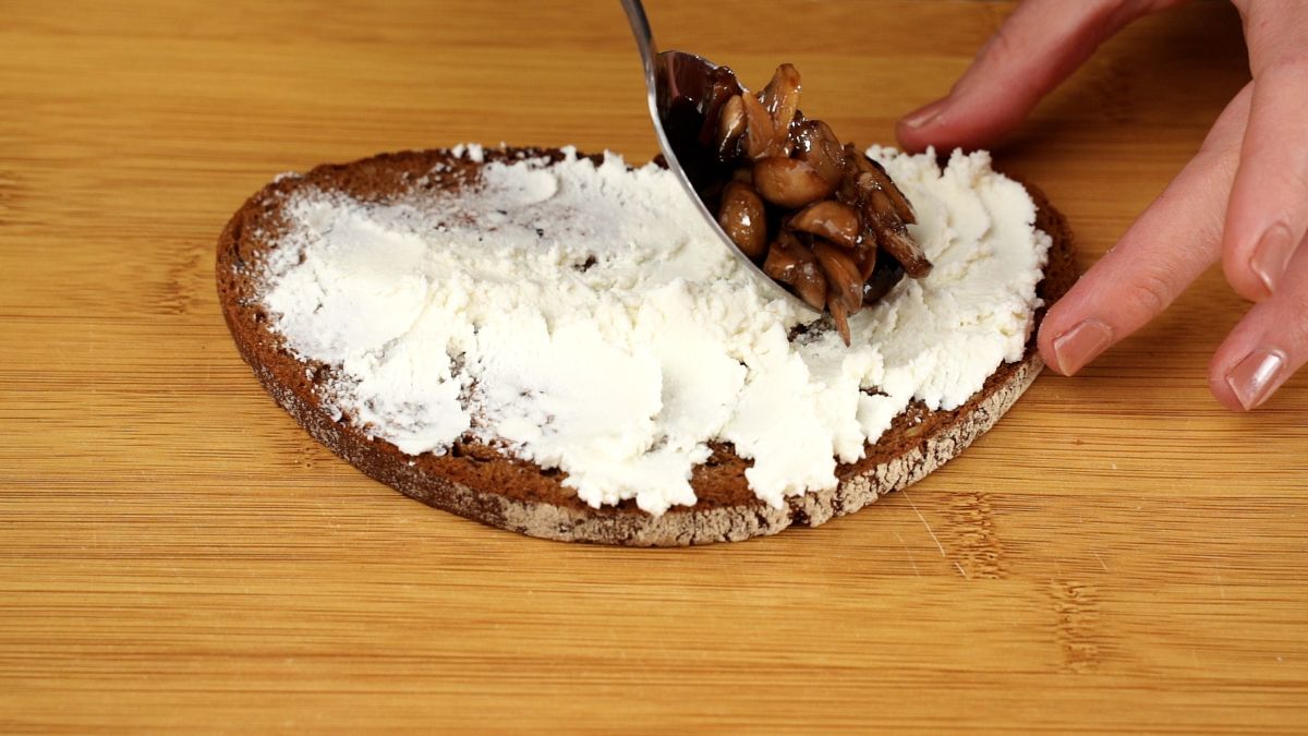 spoon of mushrooms being added to ricotta cheese on toast