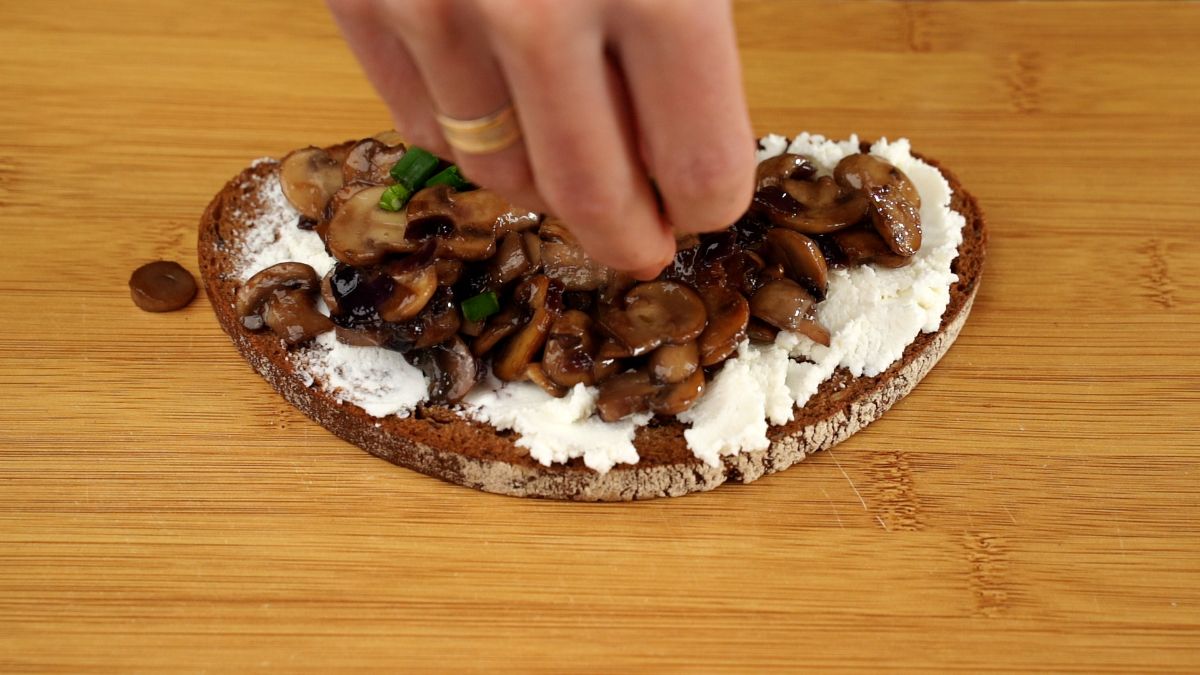 hand adding chives on top of mushrooms on toast