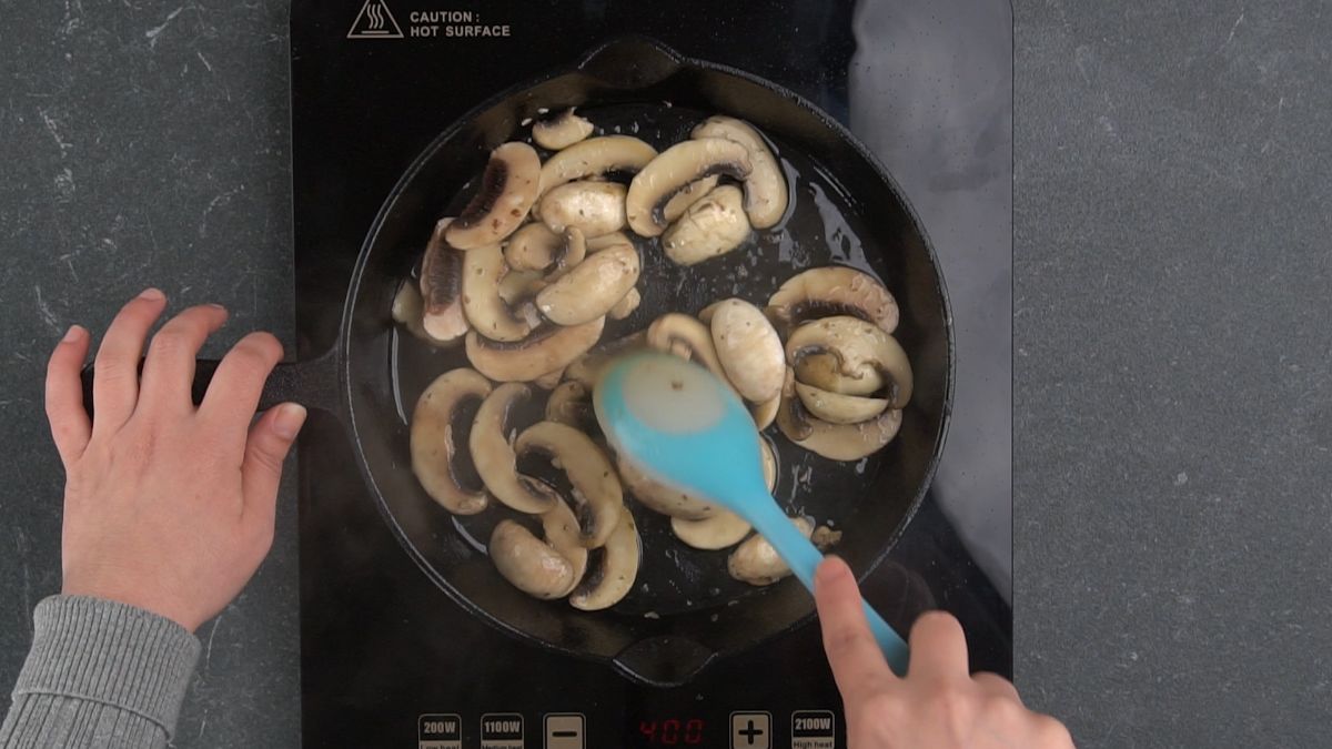 blue spoon stirring mushrooms in cast iron skillet