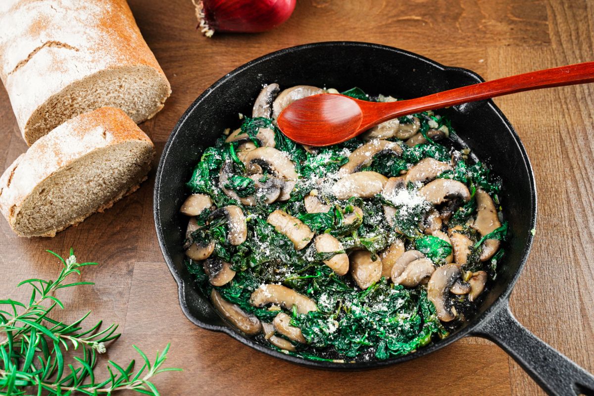 cast iron skillet filled with mushrooms and spinach with red spoon