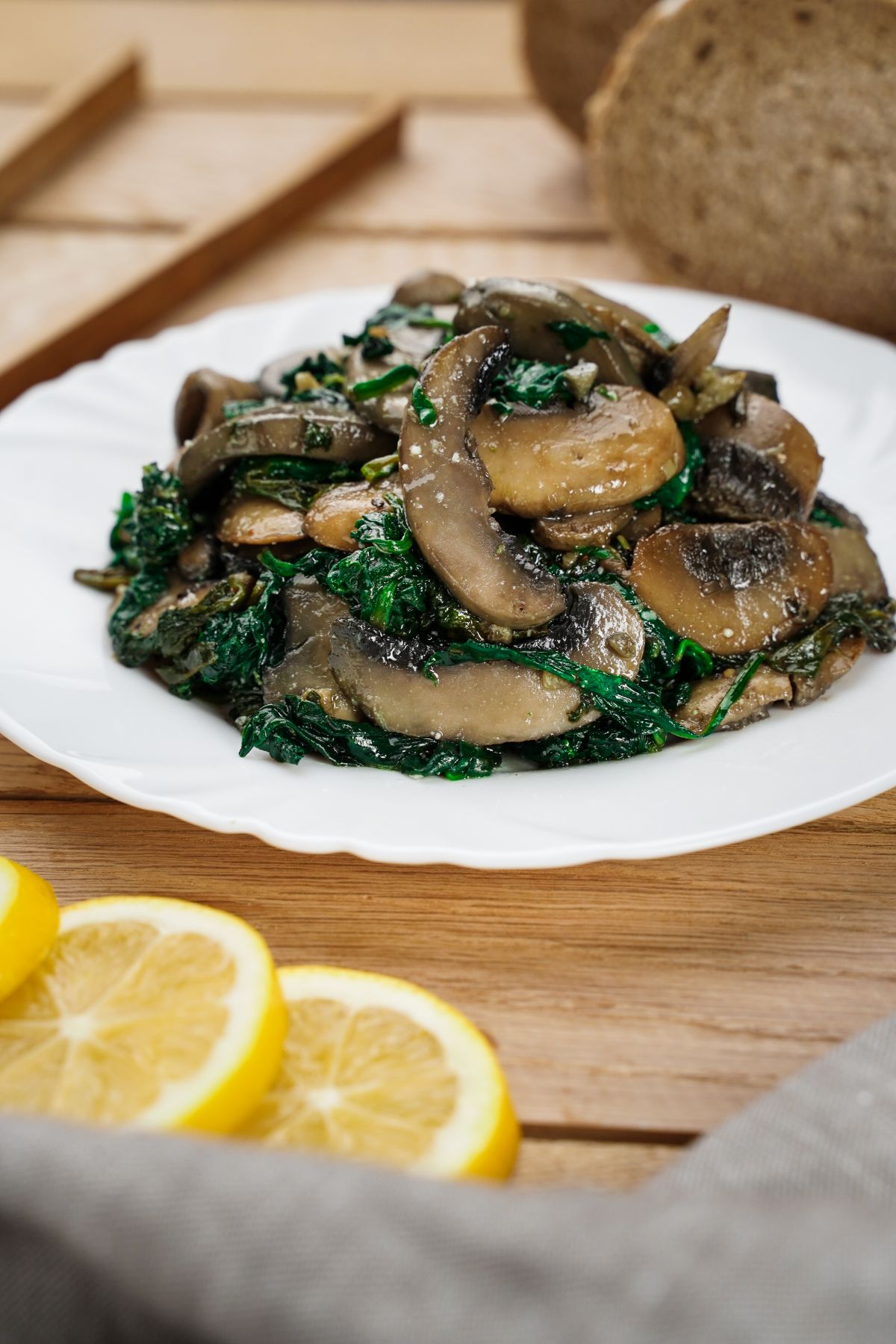 white bowl of mushrooms and spinach on table with sliced lemons by plate