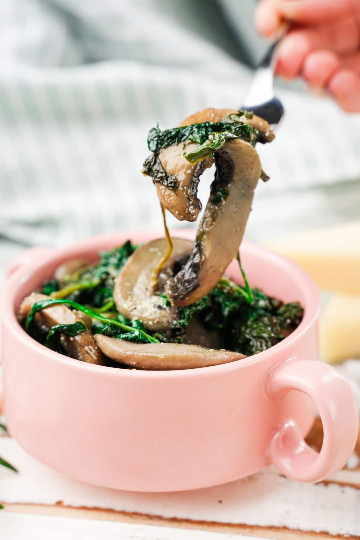 fork of mushrooms and spinach held above pink mug