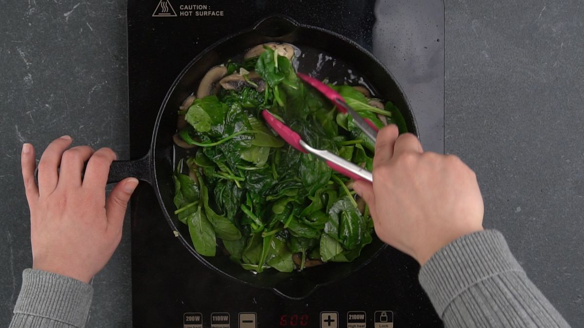pink tongs stirring spinach in skillet