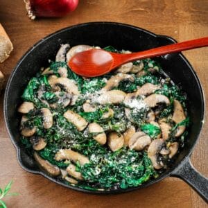 cast iron skillet filled with mushrooms and spinach with red spoon