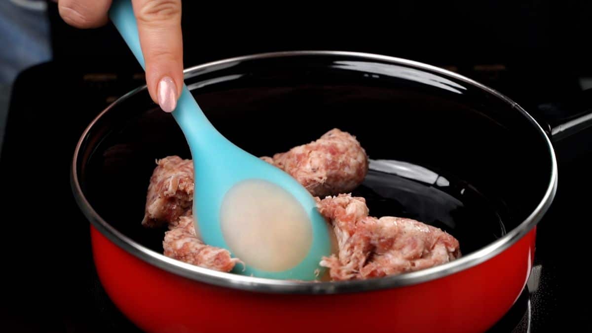 red skillet with sausage and blue spoon