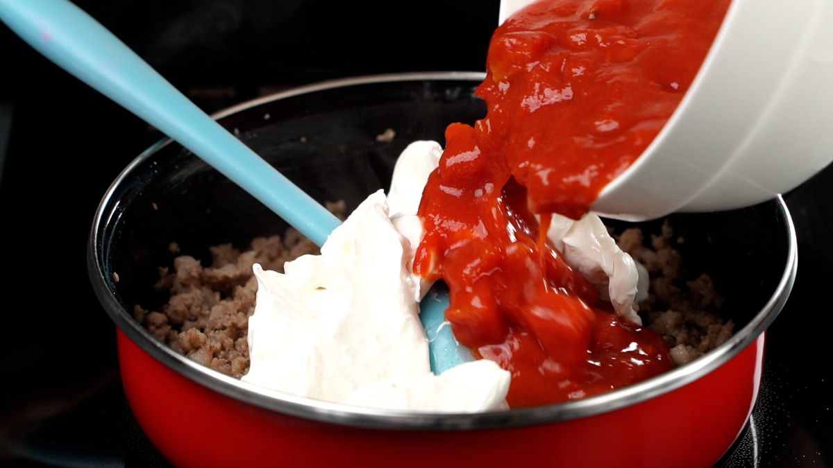 stewed tomatoes being poured into a skillet with cream cheese and sausage