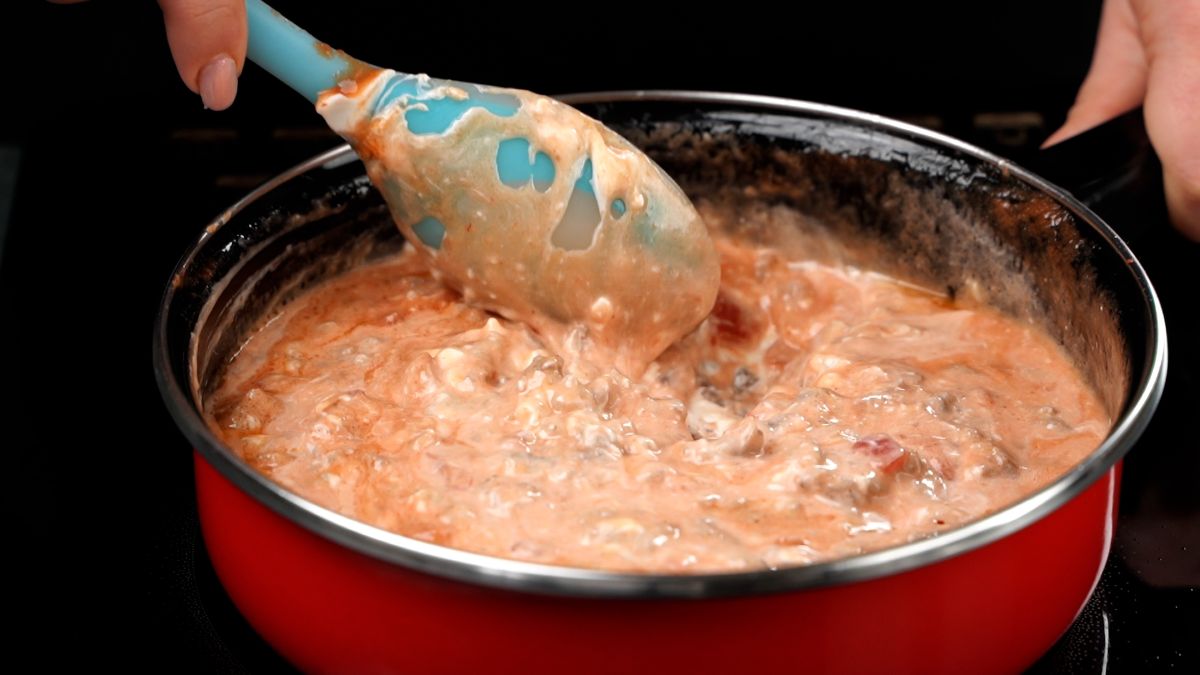 blue spoon stirring sausage dip in red skillet