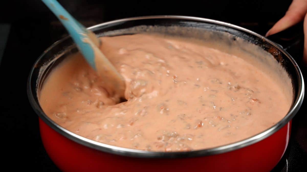 red skillet of creamy dip stirred by blue spoon