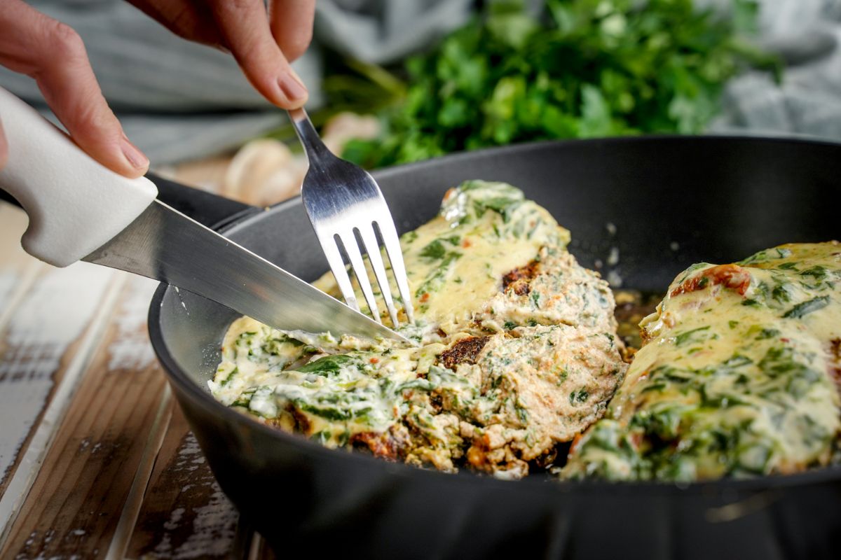 fork and knife cutting spinach stuffed chicken breasts in skillet