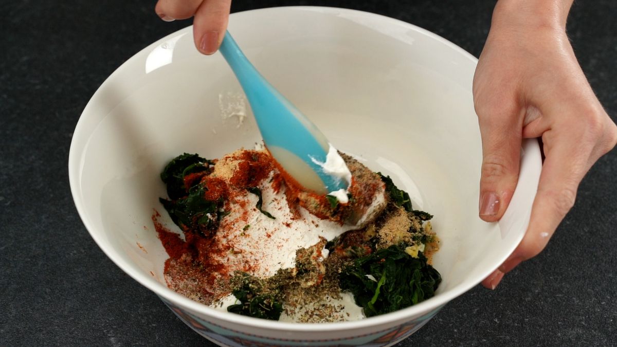 teal spoon stirring spinach and cheese with spices in white bowl