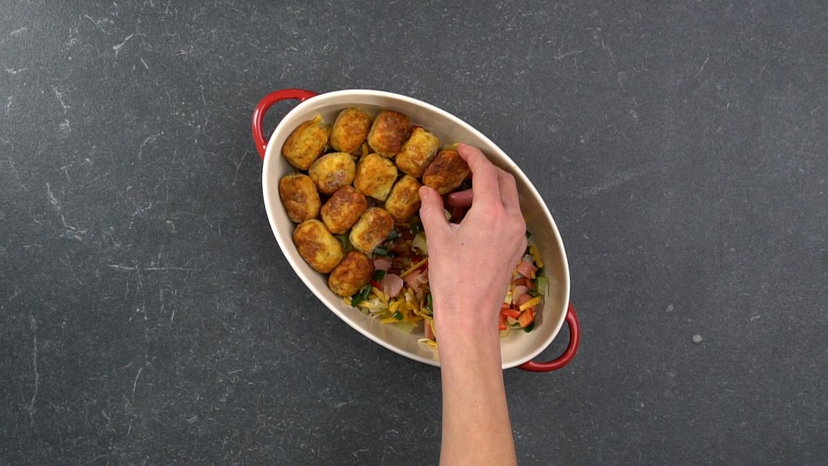 tater tots being layered on top of casserole