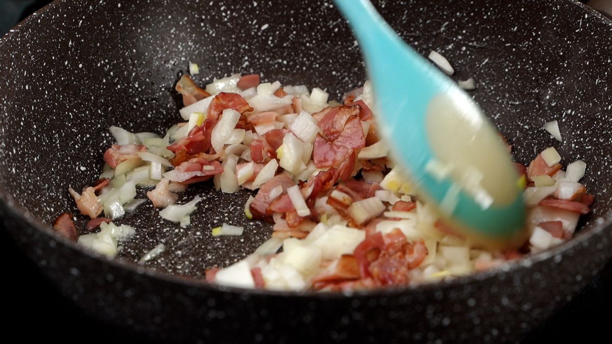 onions added to bacon being stirred by light blue spoon