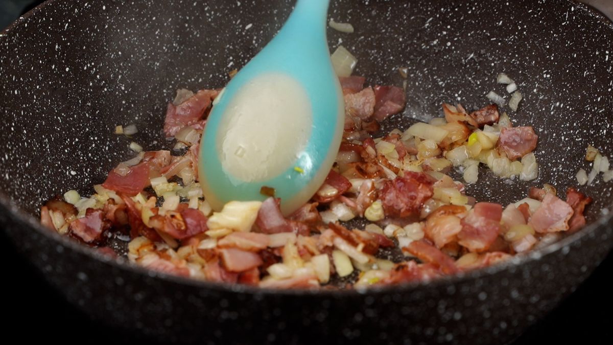 blue spoon stirring bacon and onions in skillet