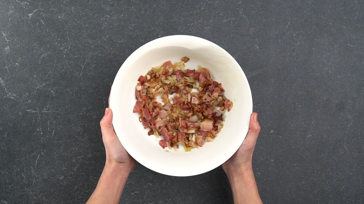 hands holding white bowl of cooked bacon