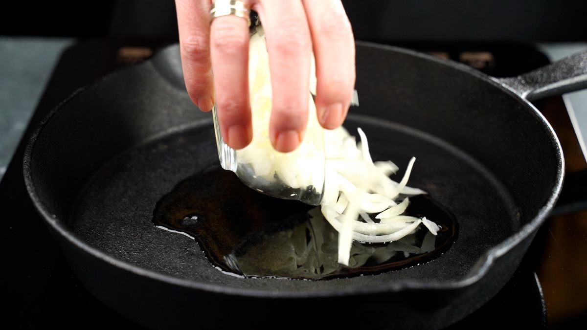 white onions being added to cast iron skillet with oil