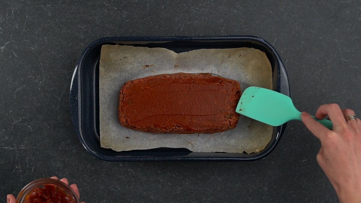 blue spoon spreading ketchup on top of meatloaf