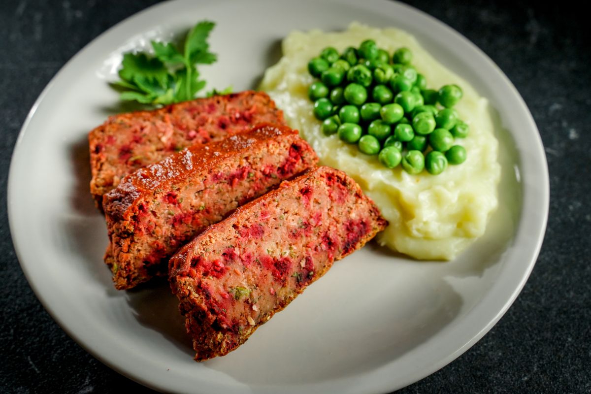 image looking down on white plate of vegan meatloaf with peas and mashed potatoes