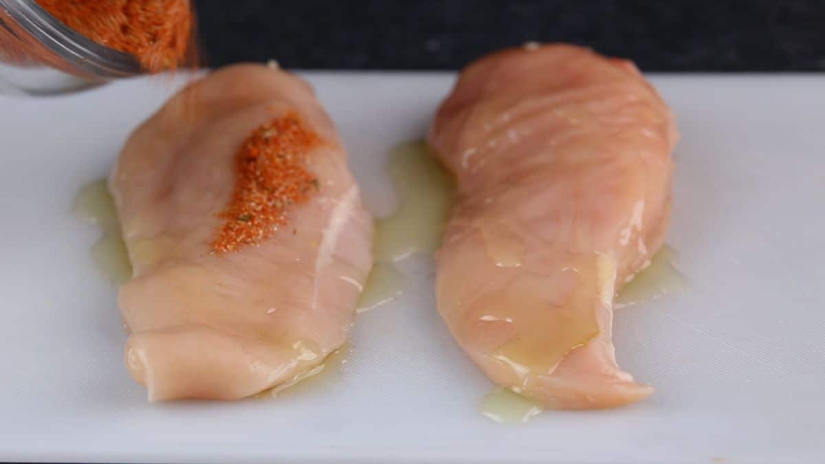 chicken breasts on white mat being seasoned