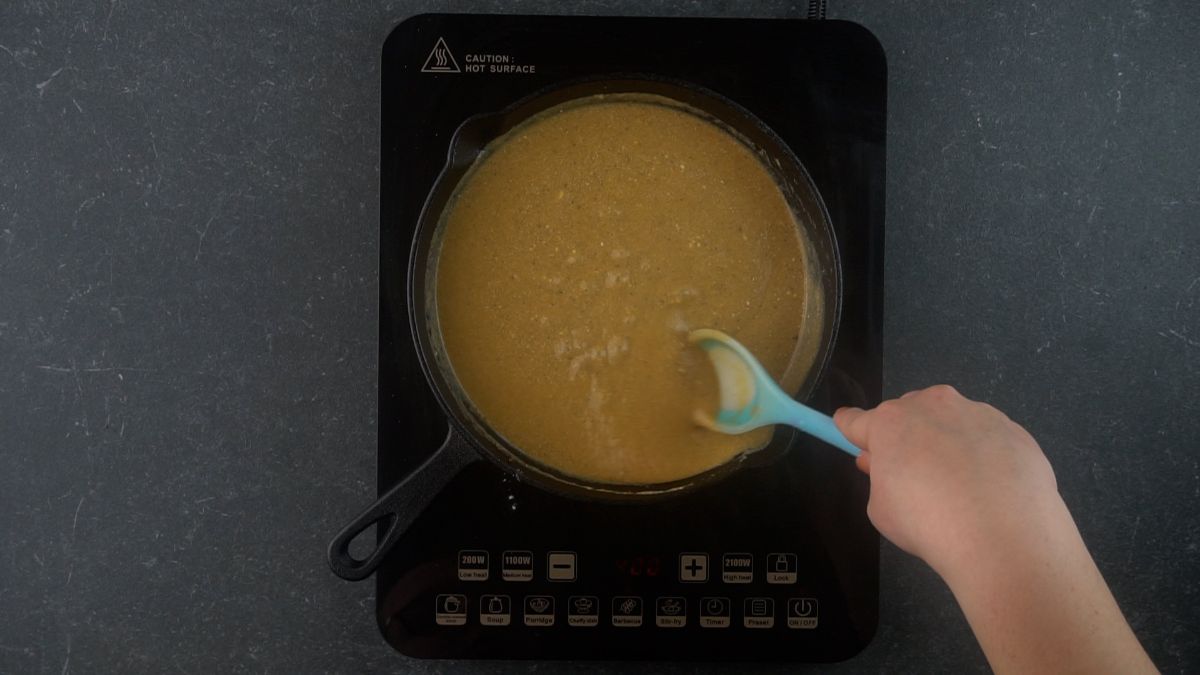 light brown sauce in skillet with light teal spoon