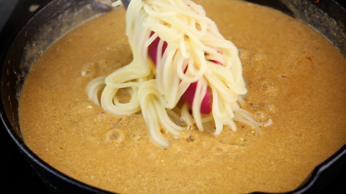 pink tongs putting pasta in sauce