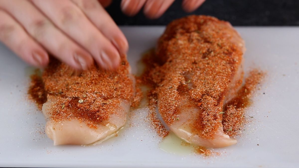 hand rubbing spice blend into chicken breasts