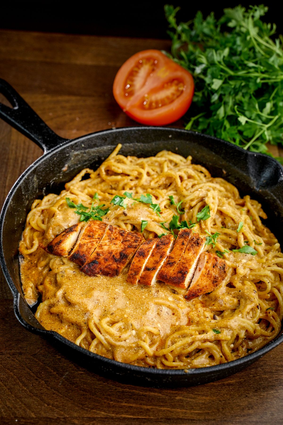 sliced tomato and herbs on table next to cast iron skillet of pasta with sliced chicken