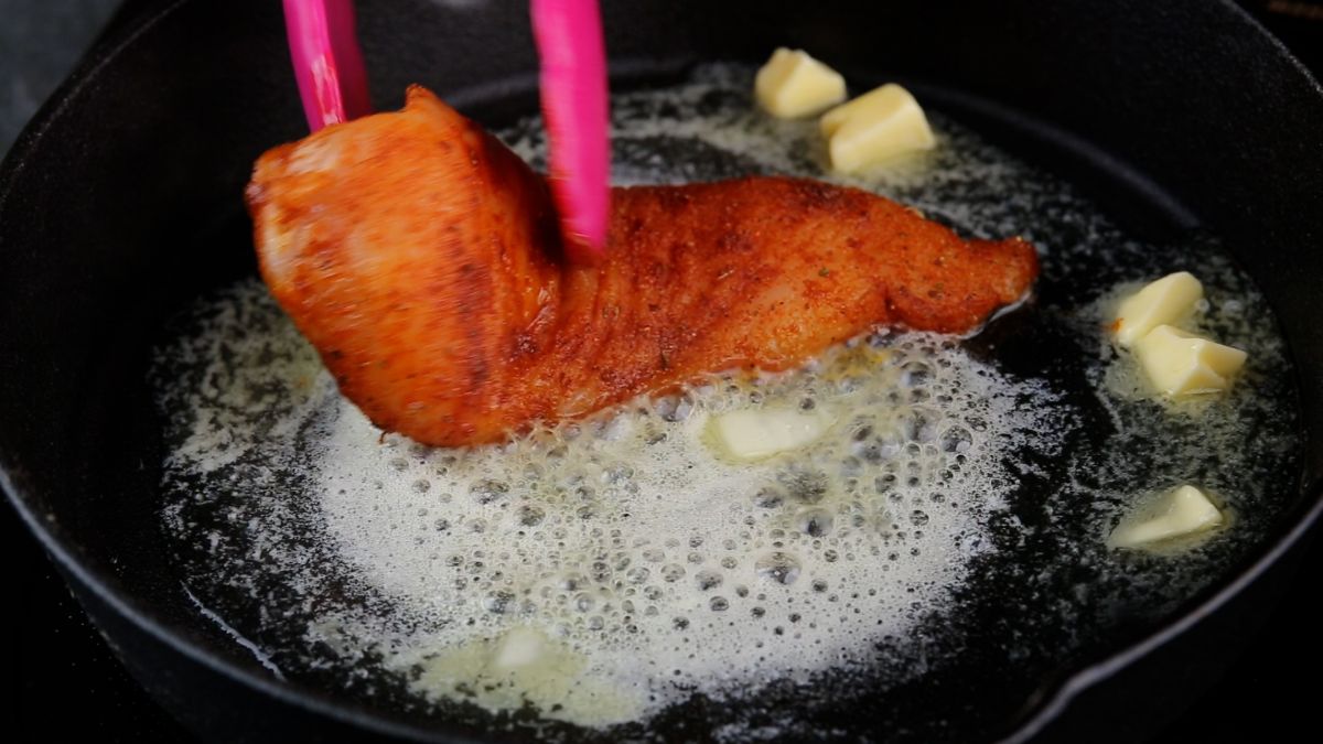 pink tongs placing chicken breast into hot skillet