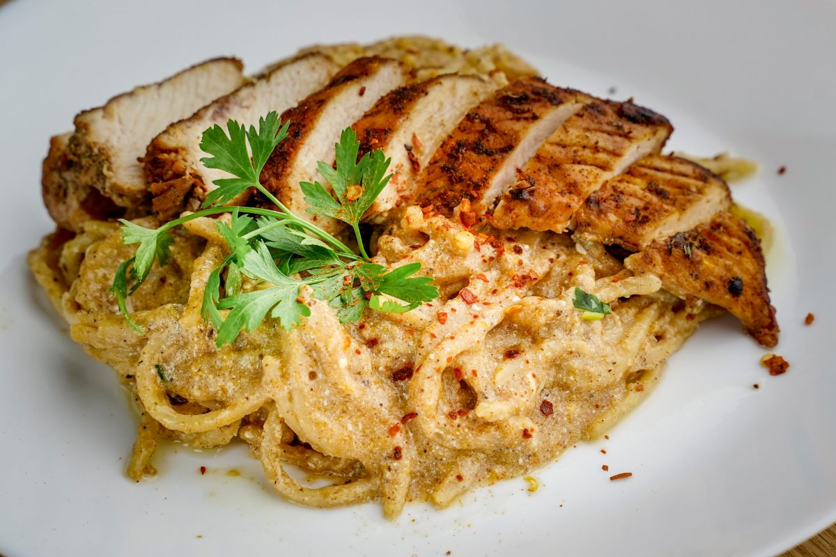 sliced cajun chicken on bed of pasta in white bowl
