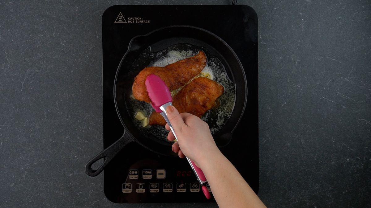 pink tongs being used to turn chicken in skillet