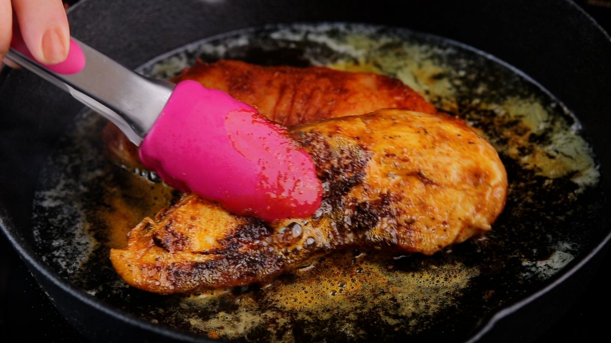 cooked chicken being removed from skillet with pink tongs