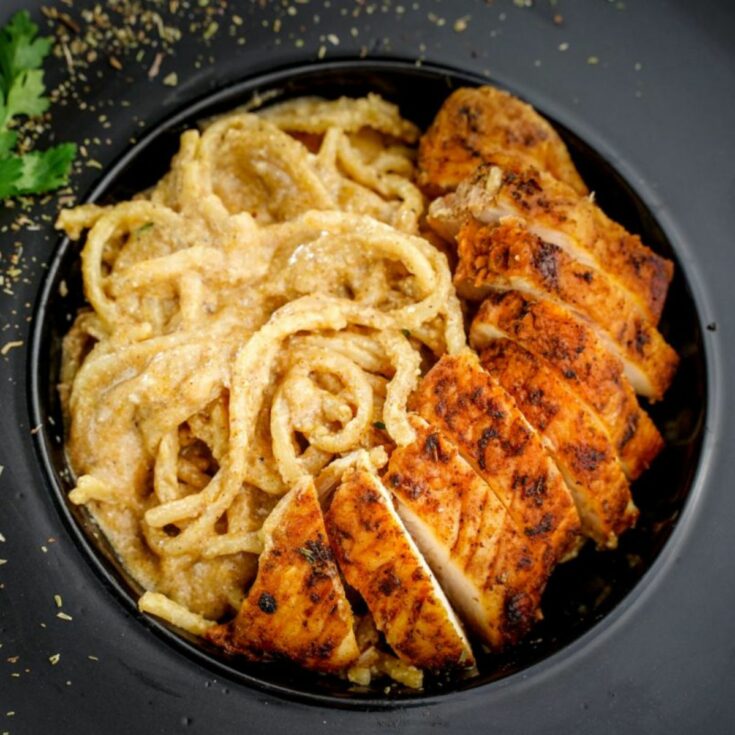 close up image of pasta with Cajun chicken on top in black bowl
