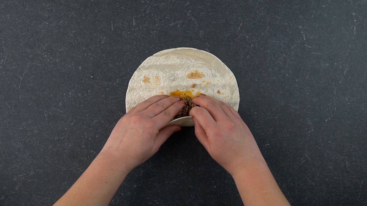 hand rolling tortilla over meat filling