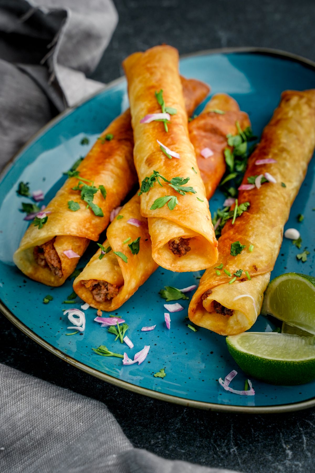 taquitos on teal plate with fresh lime wedges