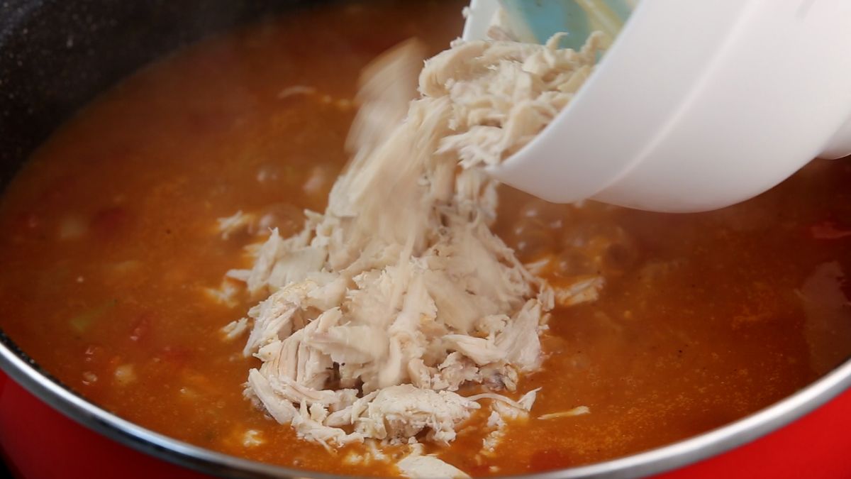 shredded chicken being added to skillet of red sauce